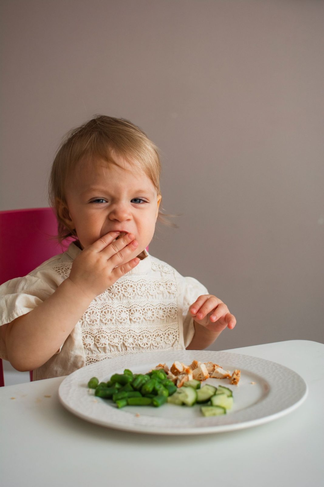 A little girl feeding herself from a plate of vegetables