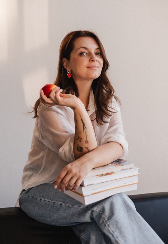 Yulia Klimanova holding an apple, with a stack of books